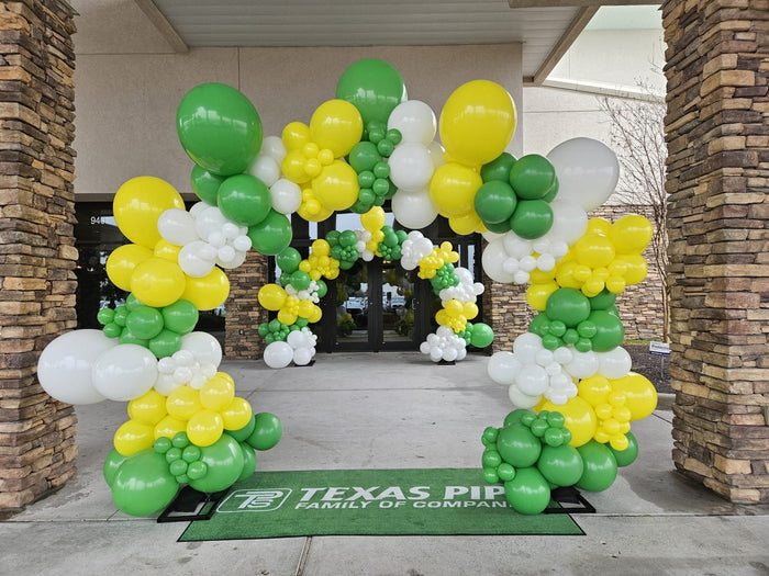 Corporate balloon arch in green, yellow and white with company logos at a Houston office entrance