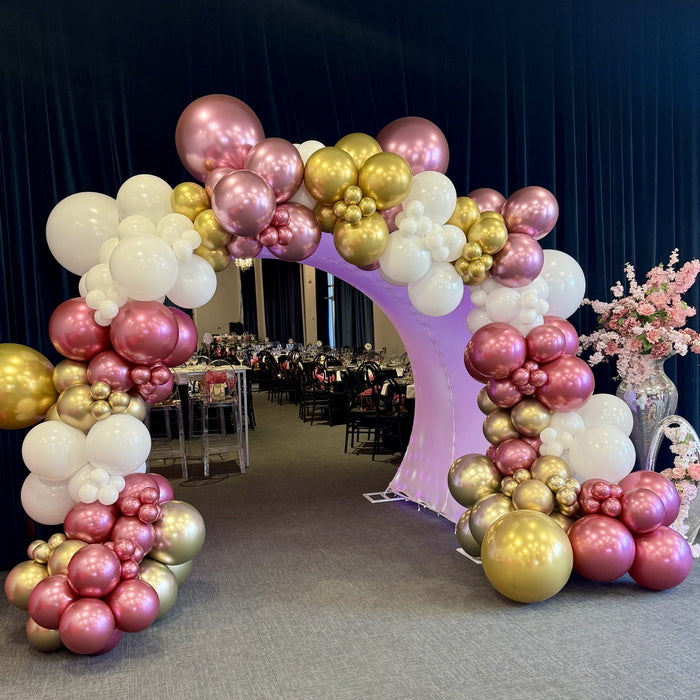 Pink and gold chrome balloon garland on a round arch backdrop at a Houston gala