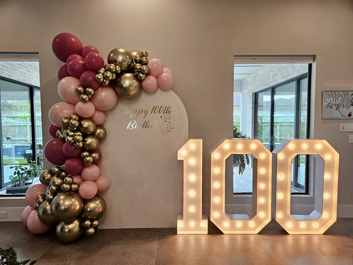 Pink and gold balloon garland with light-up 100 marquee numbers for a 100th birthday