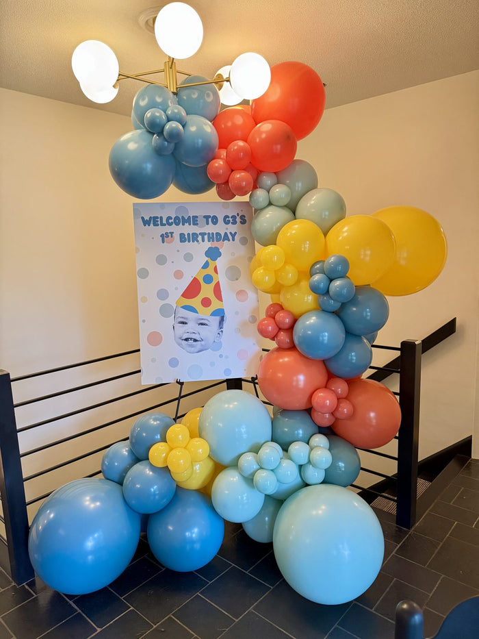 Colorful organic balloon garland around a first birthday welcome sign