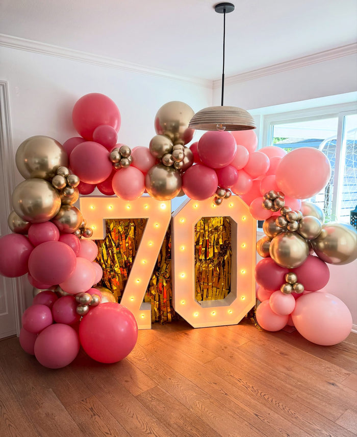 Pink and gold balloon garland with light-up 70 marquee numbers