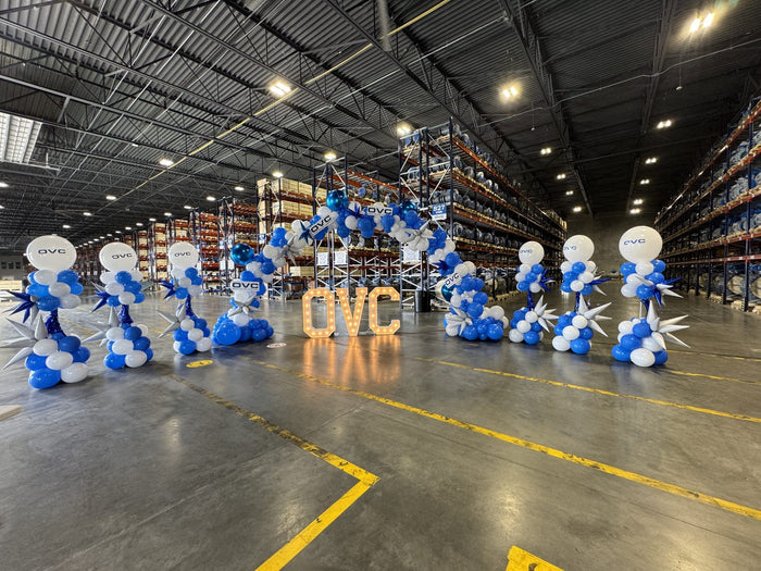 Blue and white corporate balloon columns and arch for a QVC warehouse event